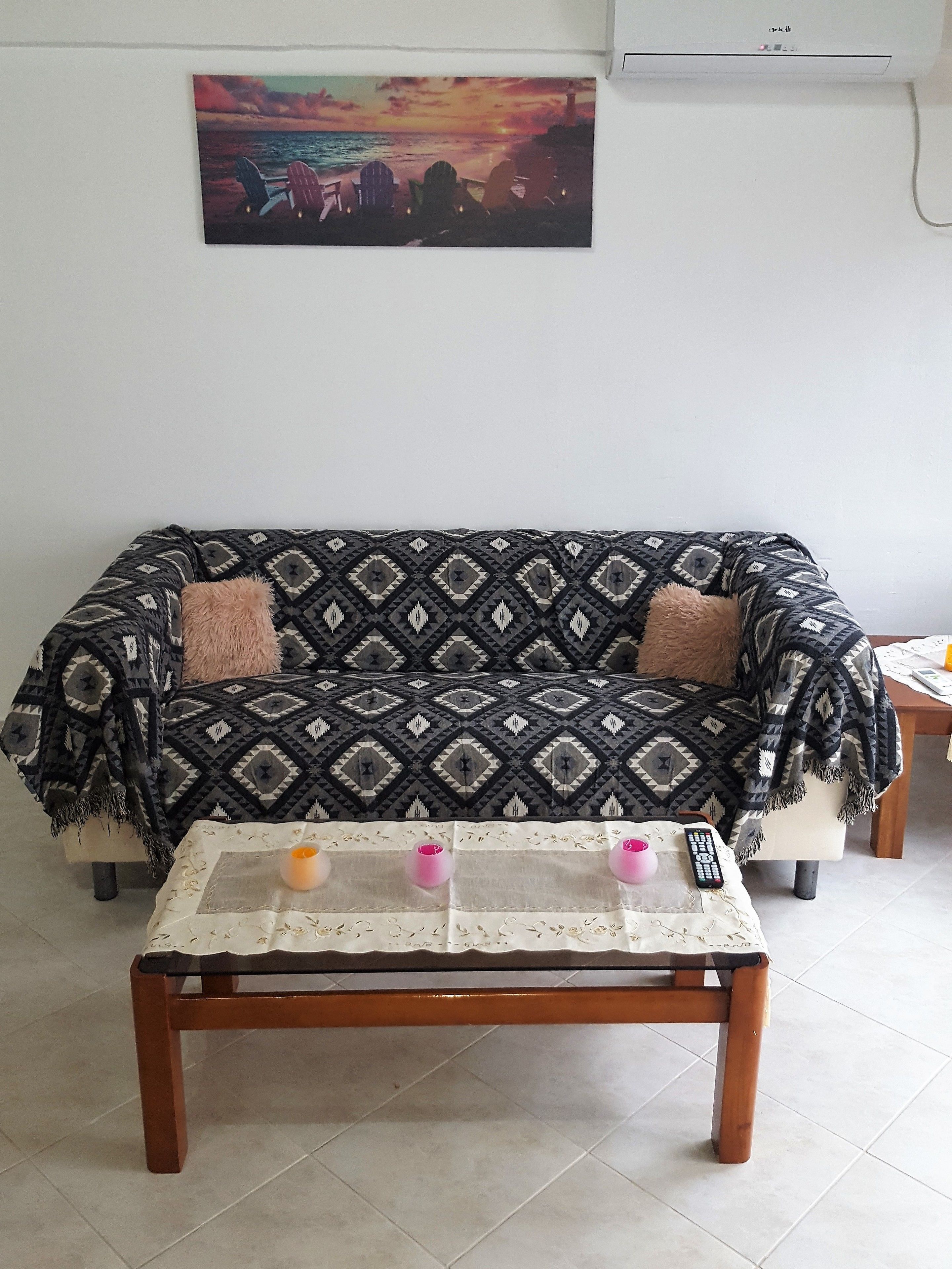 A living room with a patterned sofa, a coffee table with a lace tablecloth, and a painting on the wall.