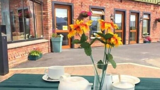 A table set with white teacups and saucers, a white teapot, and a vase with yellow flowers. - Tara View Apartments (Rathfeigh)