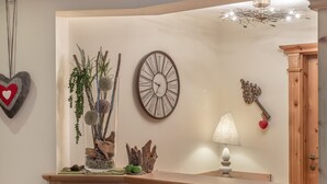 A corner of a room with a wooden cabinet, a wall clock, a decorative vase with plants, and a lamp. - Residenz Allegra (Soelden)