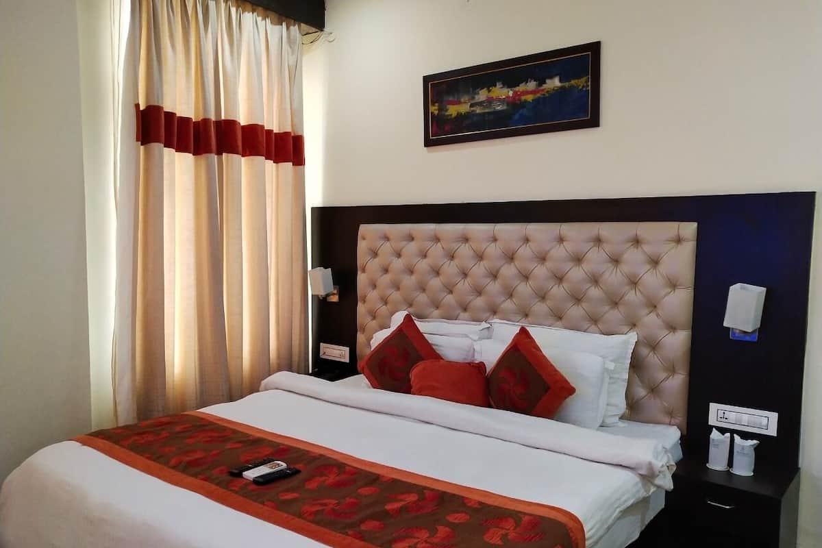 A hotel room with a large bed, a headboard, a nightstand, a bedside table, a wall-mounted phone, and a painting on the wall.