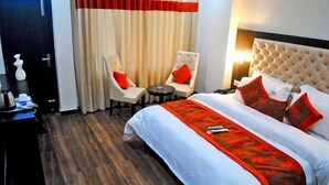 A hotel room with a large bed, two armchairs, a small round table, and a nightstand with a lamp. - Hotel Triund Heights (Dharamshala)