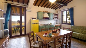 Un comedor con una mesa y sillas de madera, un sofá verde y una cocina al fondo.