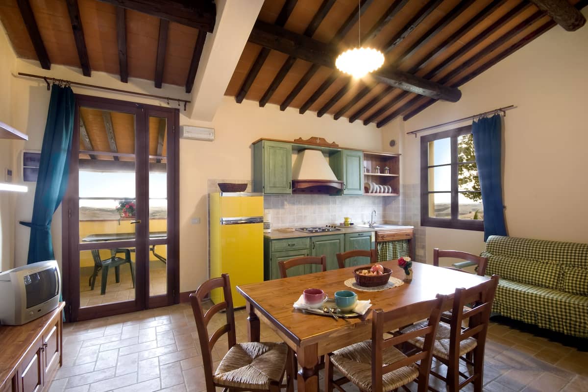 A dining area with a wooden table and chairs, a green sofa, and a kitchen in the background.
