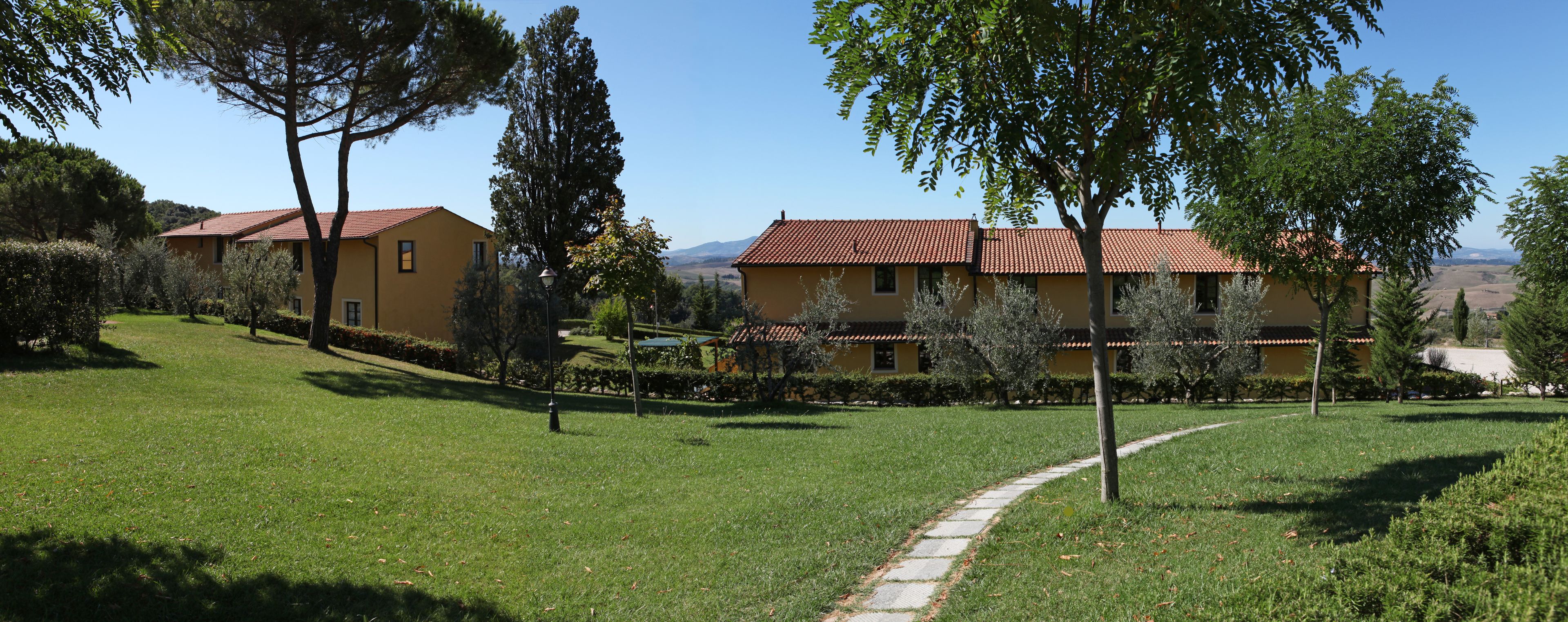 A yellow building with a red roof, surrounded by green grass and trees.