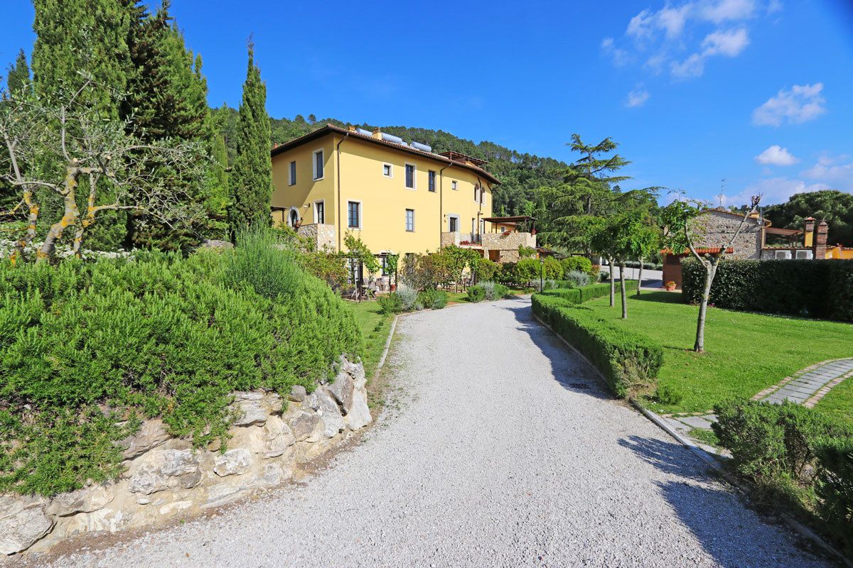 A yellow building with a gravel driveway leading to a paved path.