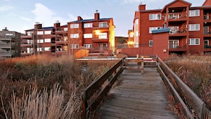 A wooden boardwalk leading to a multi-story residential building with balconies and a clear sky. - Cinnamon Ridge B304 by SummitCove Vacation Lodging (Keystone)