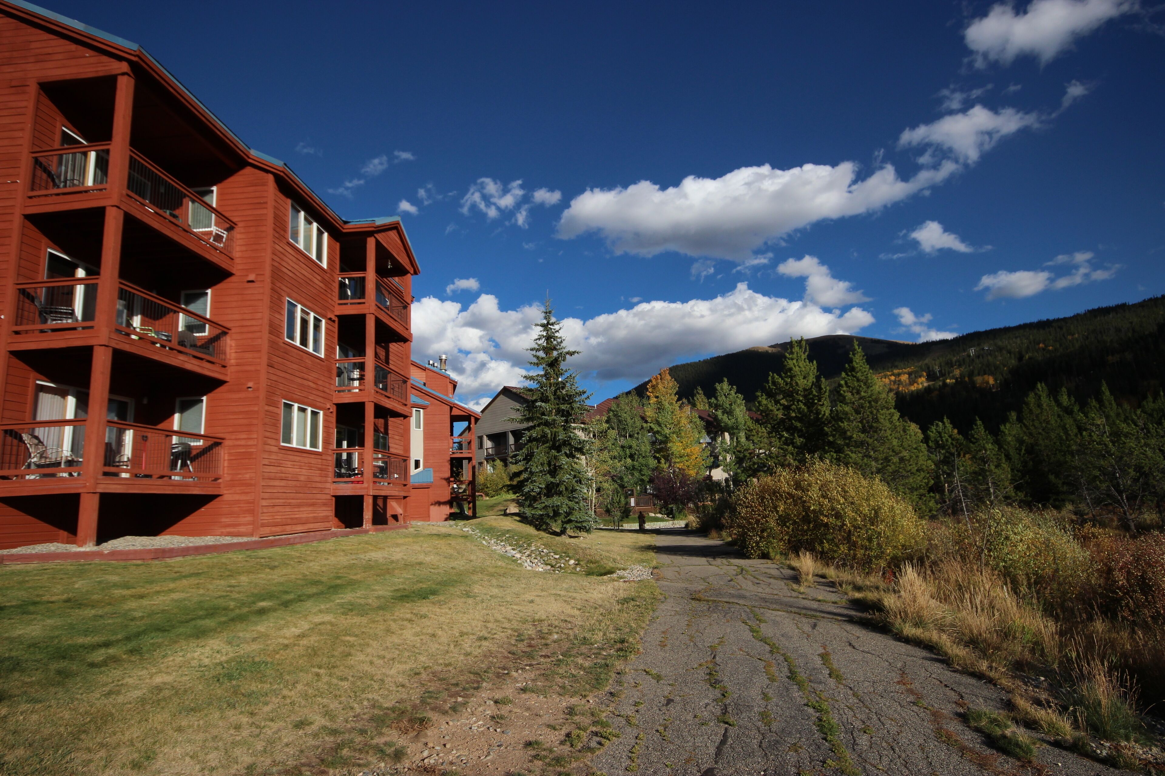 A red multi-story building with balconies, a paved driveway, and a mountainous backdrop.