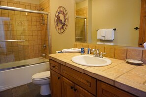 A bathroom with a glass-enclosed shower, a white sink, wooden cabinets, and a decorative wall piece. - Seasons 1851 (Keystone)