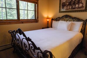 A neatly made bed with a headboard, a bedside lamp, and a window with a view of trees. - Seasons 1851 (Keystone)