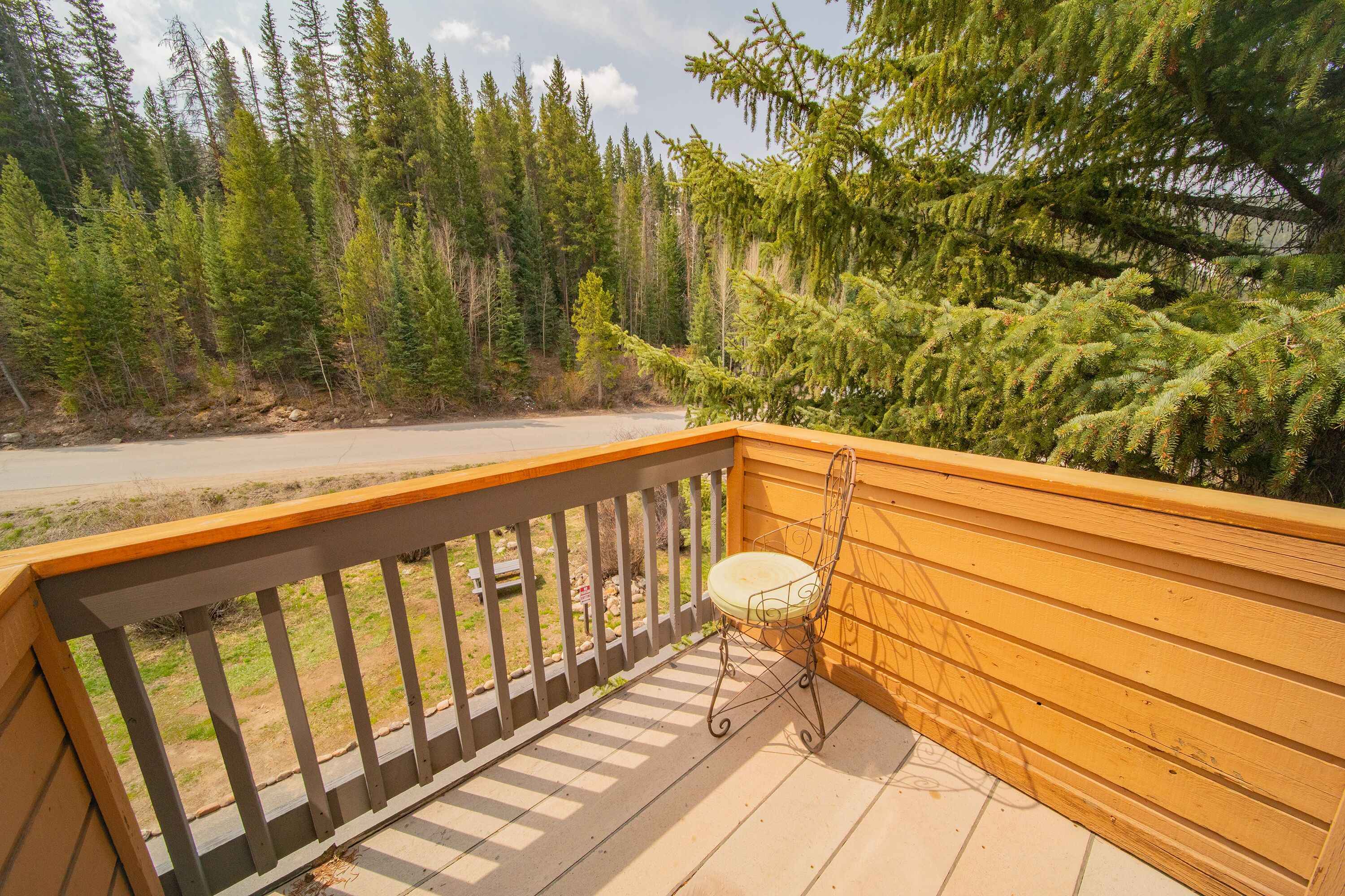 Une terrasse en bois avec une chaise en métal et une vue sur une zone boisée.