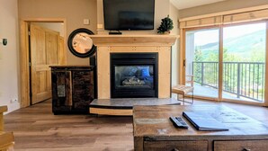 A living room with a fireplace, a television mounted above it, and a view of a balcony with a scenic landscape. - Silver Mill 8226 (Keystone)