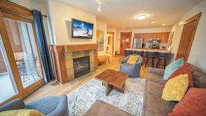 A modern living room with a fireplace, a television, and a kitchen area in the background. - Springs 8838 (Keystone)