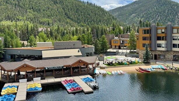 Un hôtel situé au bord d’un lac, doté d’un quai, de pédalos aux couleurs vives et surplombant un paysage montagneux.