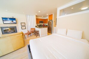 A hotel room with a large bed, a TV mounted on the wall, a kitchen area with a microwave and refrigerator, and a seating area with a sofa and chairs.