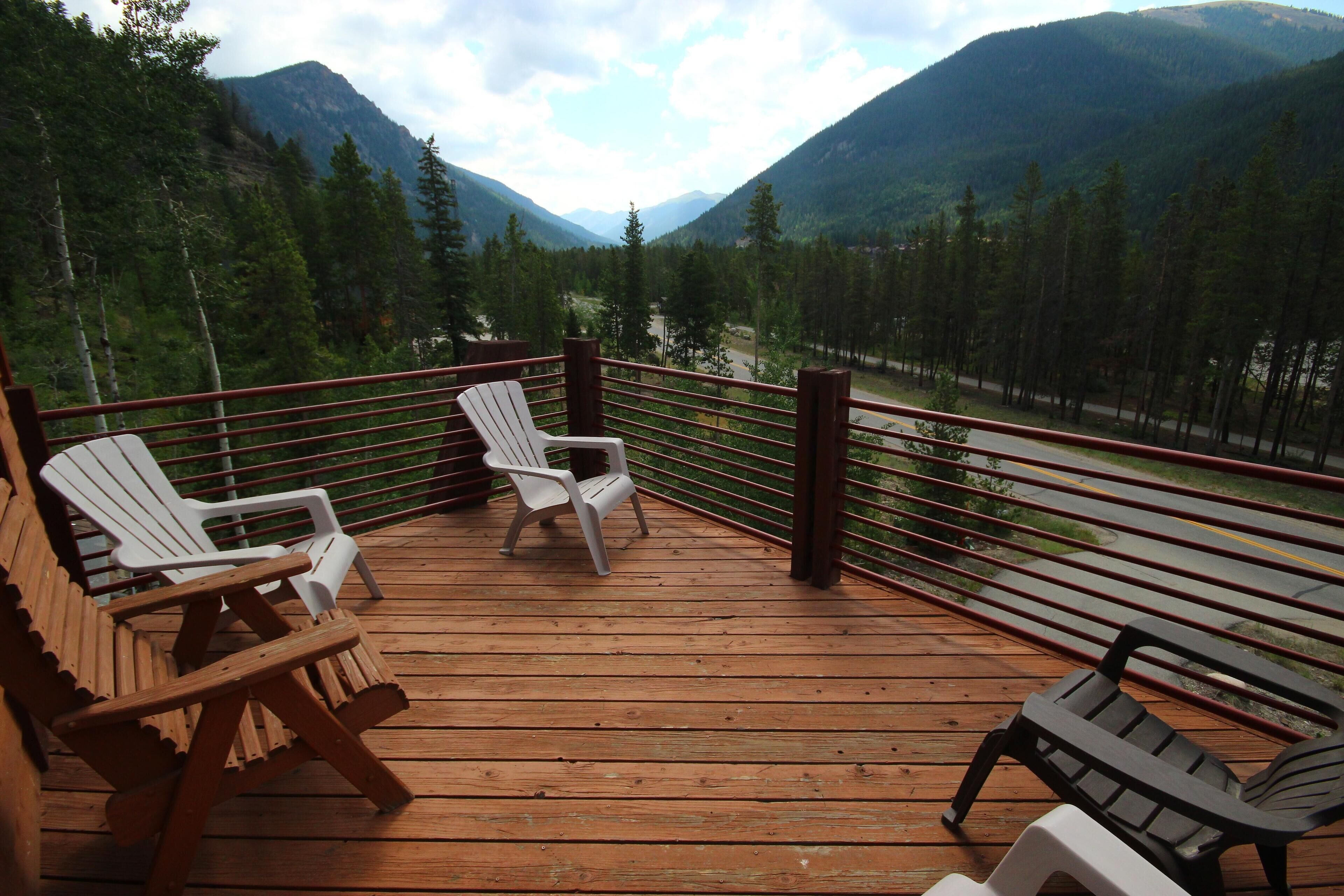 A wooden deck with Adirondack chairs overlooking a forested valley and mountains.