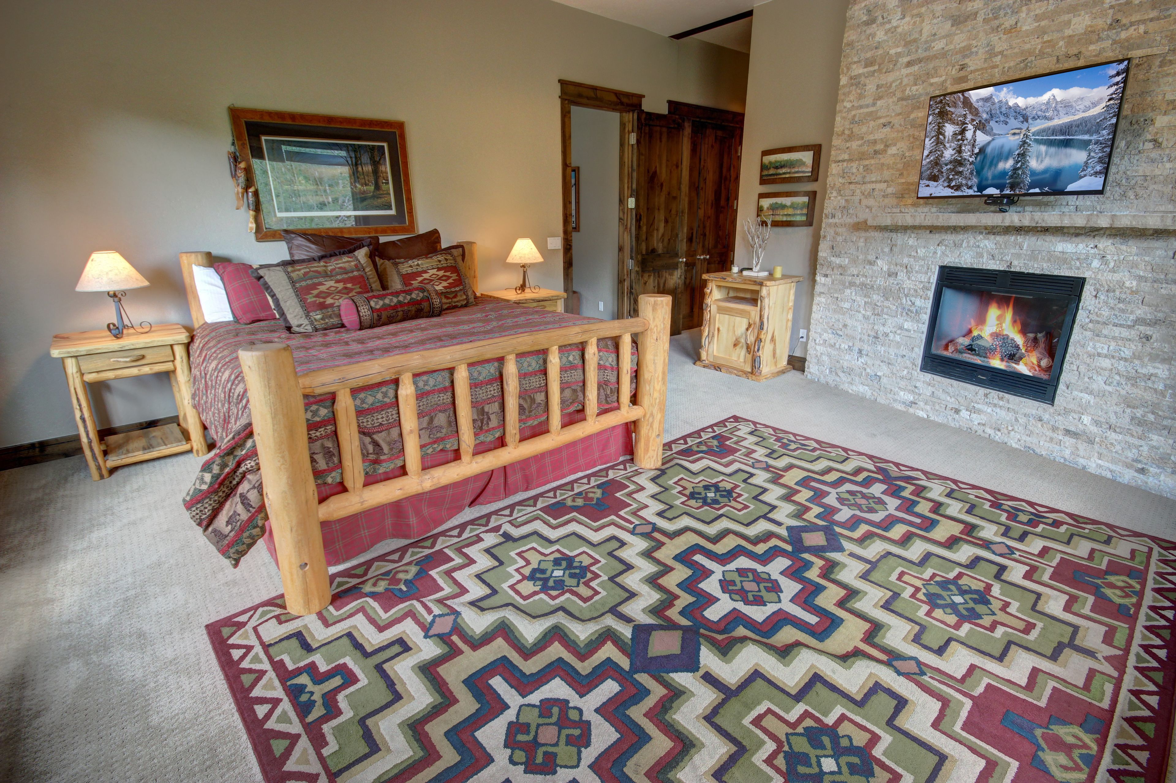 A cozy bedroom with a wooden bed, patterned rug, and a fireplace.