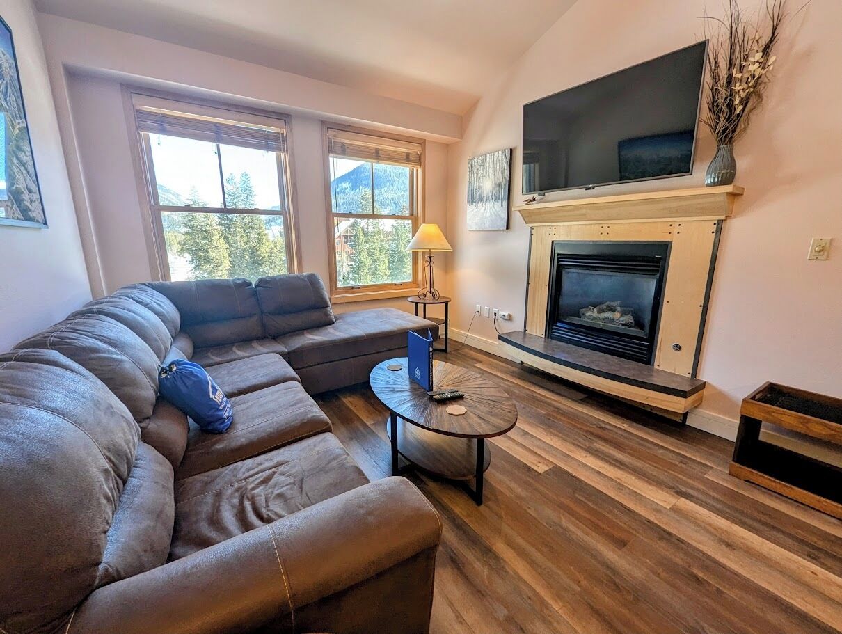 Una sala de estar con un sofá modular, una chimenea y un televisor montado encima.