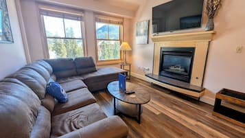 Una sala de estar con un sofá modular, una chimenea y un televisor montado encima.