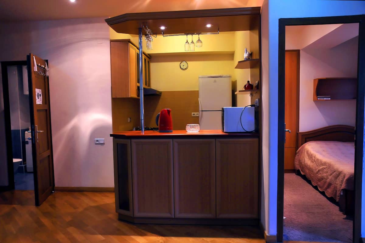 Une cuisine compacte avec des meubles en bois, un réfrigérateur, une machine à café et une horloge au mur.