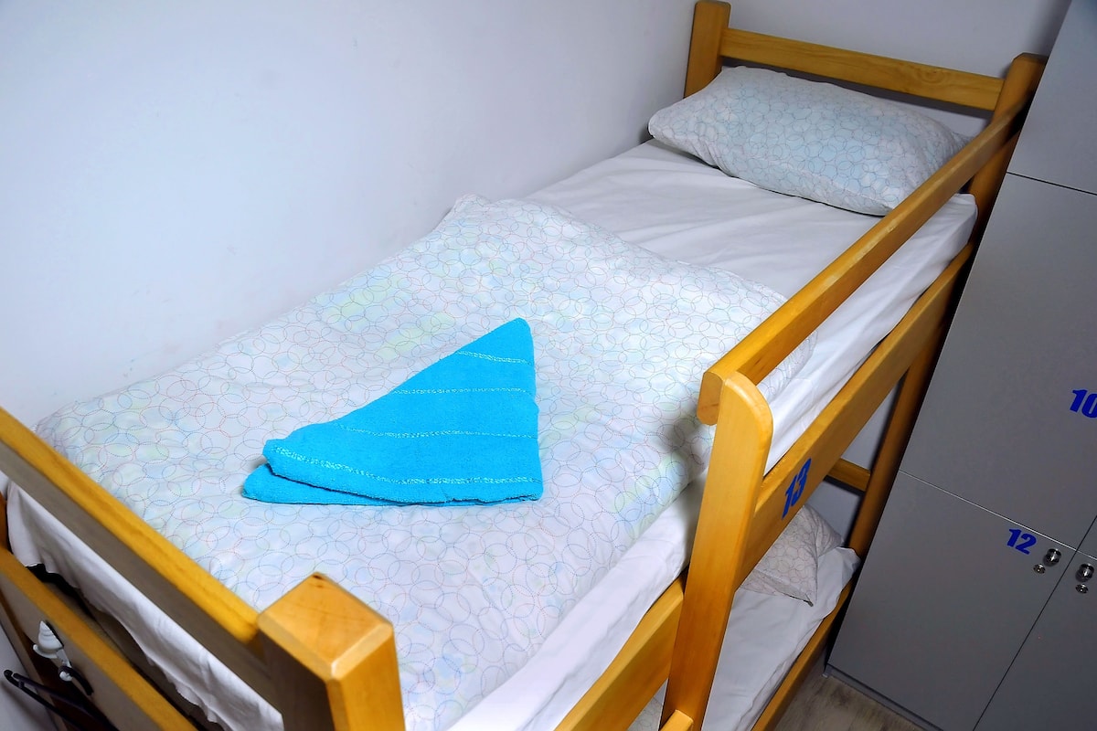 Un simple lit superposé en bois, avec un matelas à motifs et une serviette bleue sur le lit du haut.