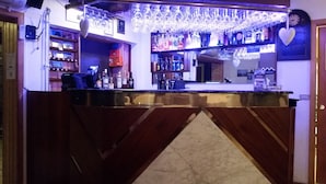 A bar area with a counter, shelves with bottles, and hanging glasses.