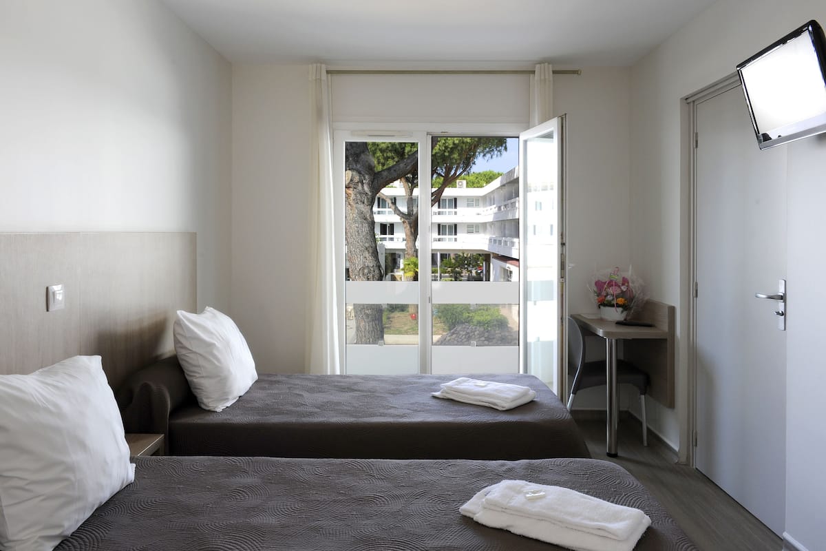 Habitación de hotel con dos camas, un escritorio y vistas a un edificio y árboles.