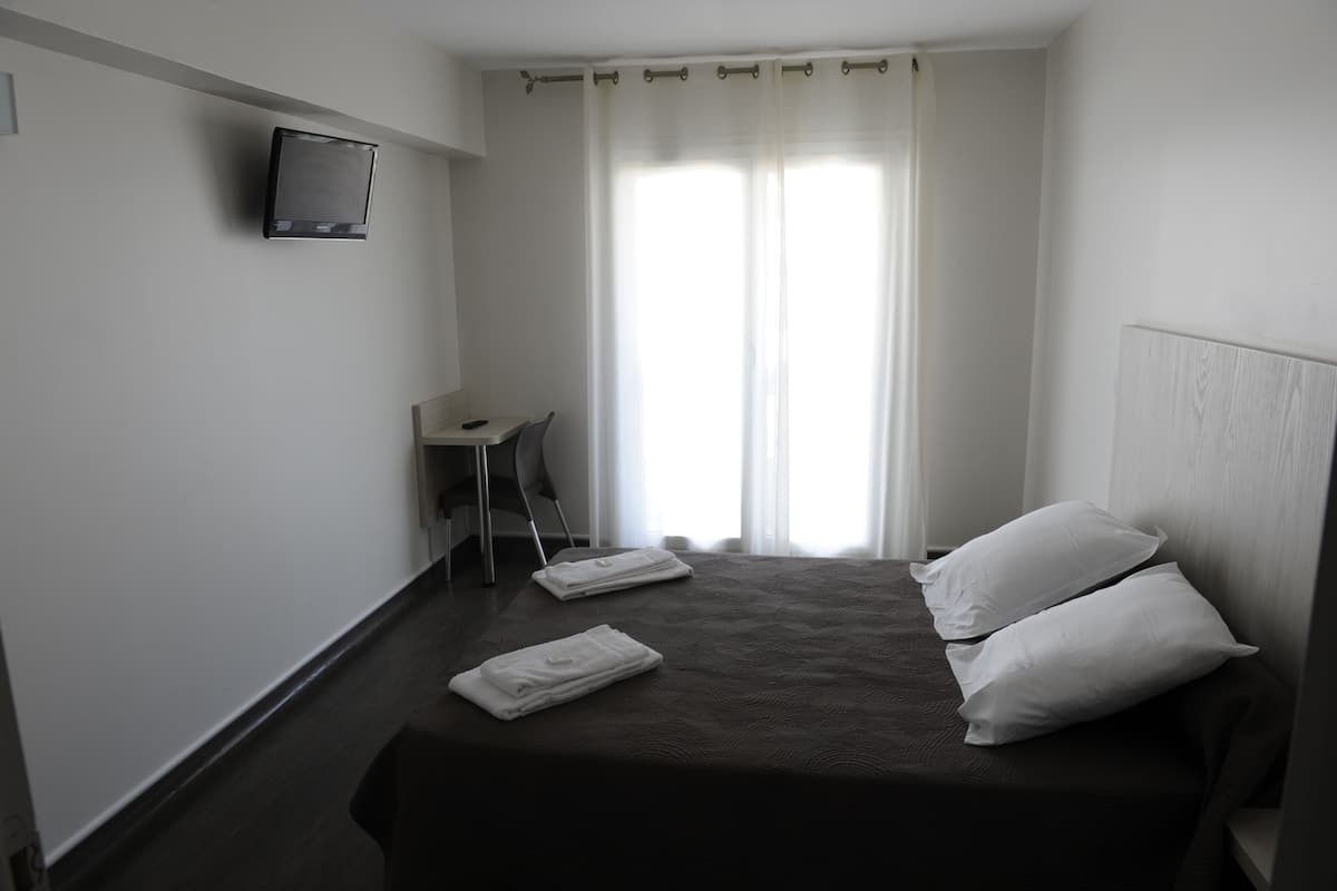 Habitación de hotel con cama, dos almohadas, televisor montado en la pared, escritorio y una silla.