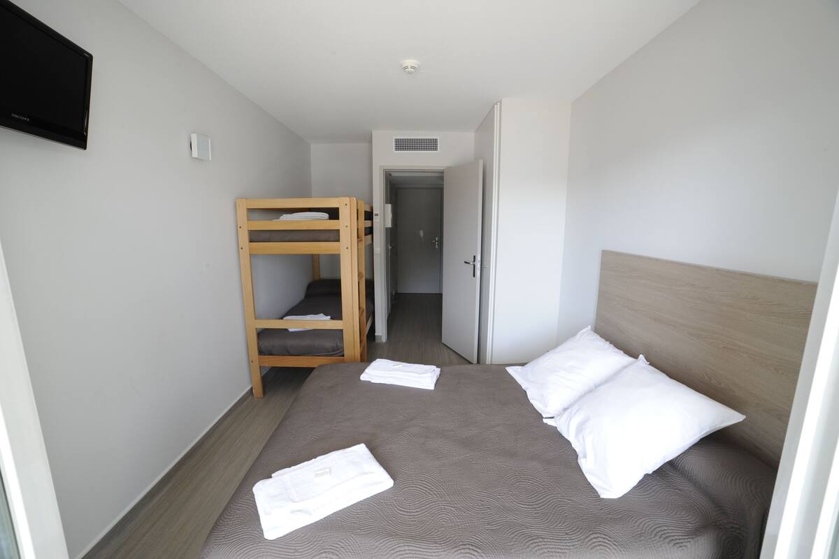 Una habitación de hotel con una cama litera, una cama individual, un televisor de pantalla plana y una puerta que da a otra habitación.