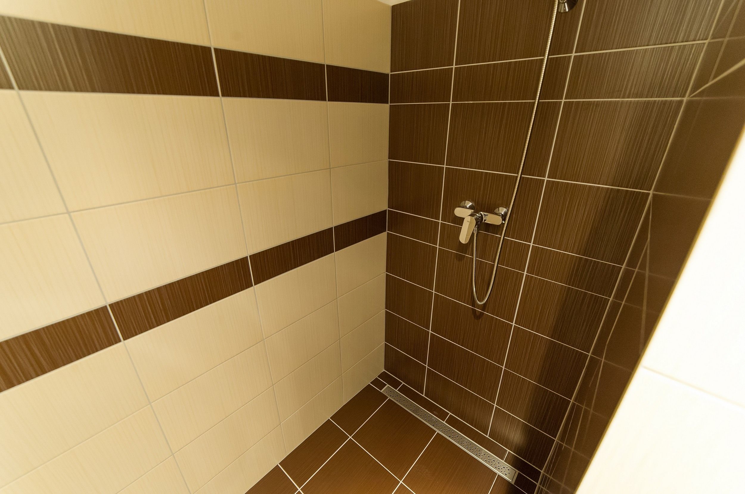 Un espace douche avec des murs et un sol carrelés, une pomme de douche et un pommeau de douche amovible.