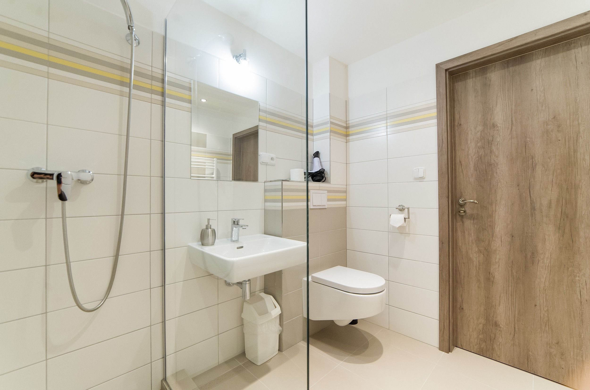 Moderni kylpyhuone, jossa on lasinen suihkuseinä, valkoinen pesuallas ja wc-istuin.