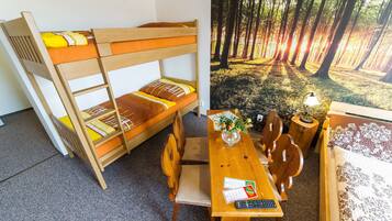 Uma cama de beliche com estrutura de madeira e roupa de cama laranja, uma mesa de jantar de madeira com cadeiras e uma pequena mesa de apoio com um abajur e flores.