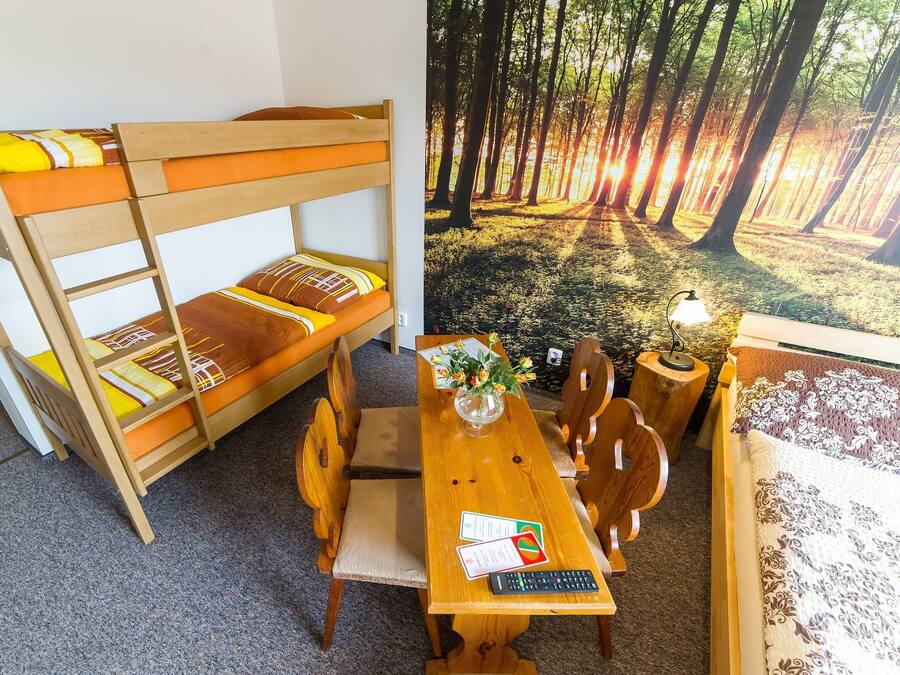Uma cama de beliche com estrutura de madeira e roupa de cama laranja, uma mesa de jantar de madeira com cadeiras e uma pequena mesa de apoio com um abajur e flores.