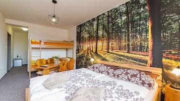 Un dormitorio con una cama litera, un amplio mural con motivos forestales, un escritorio de madera con sillas y una mesita de noche con lámpara.