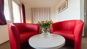A room with two red leather sofas, a white round table, and a vase with flowers. - Penzion Top (Cesky Krumlov)