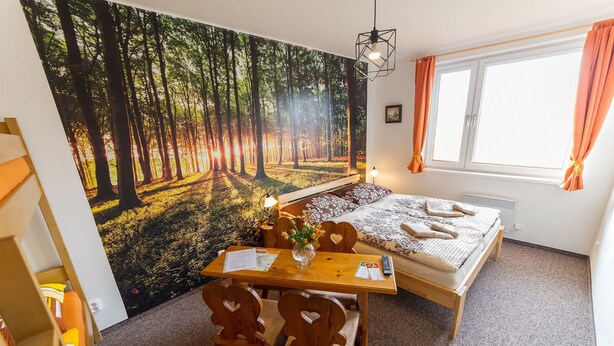 A bedroom with a bed, a desk, and a chair. There is a window with curtains and a painting of a forest on the wall. - Penzion Top (Cesky Krumlov)