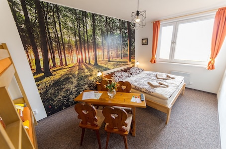A bedroom with a bed, a desk, and a chair. There is a window with curtains and a painting of a forest on the wall.