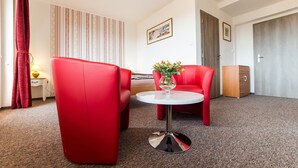 A hotel room with two red chairs, a white table with a vase of flowers, a lamp, a striped wall, and a framed picture. - Penzion Top (Cesky Krumlov)