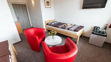 Una habitación pequeña y moderna con una cama, un televisor, una mesita con flores y sillas rojas.