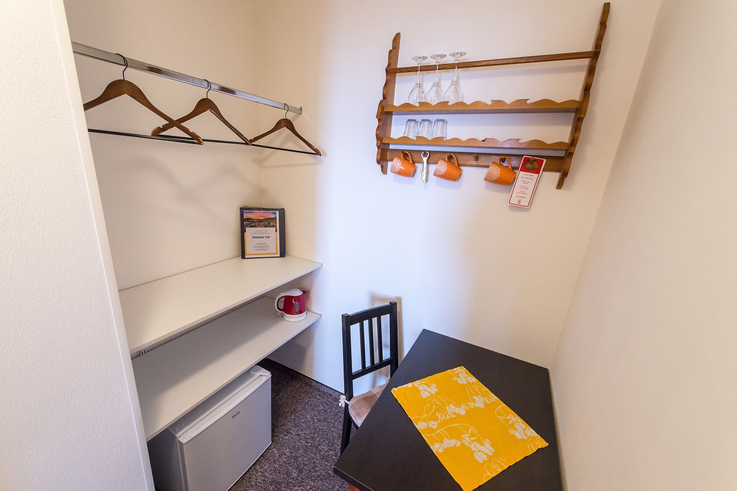 A small room with a desk, chair, and a shelf with mugs and glasses.