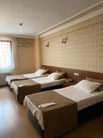 Habitación de hotel con cuatro camas individuales, cabecero de madera, ventana con cortinas y pared con diseño.