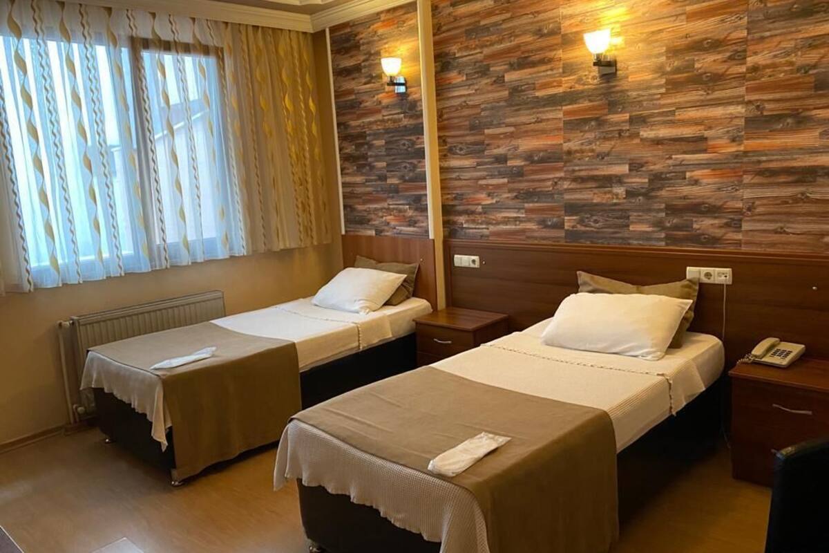 Ein Hotelzimmer mit zwei Einzelbetten, Holzwandverkleidung, Nachttischlampen, einem Heizkörper und einem Telefon auf dem Nachttisch.
