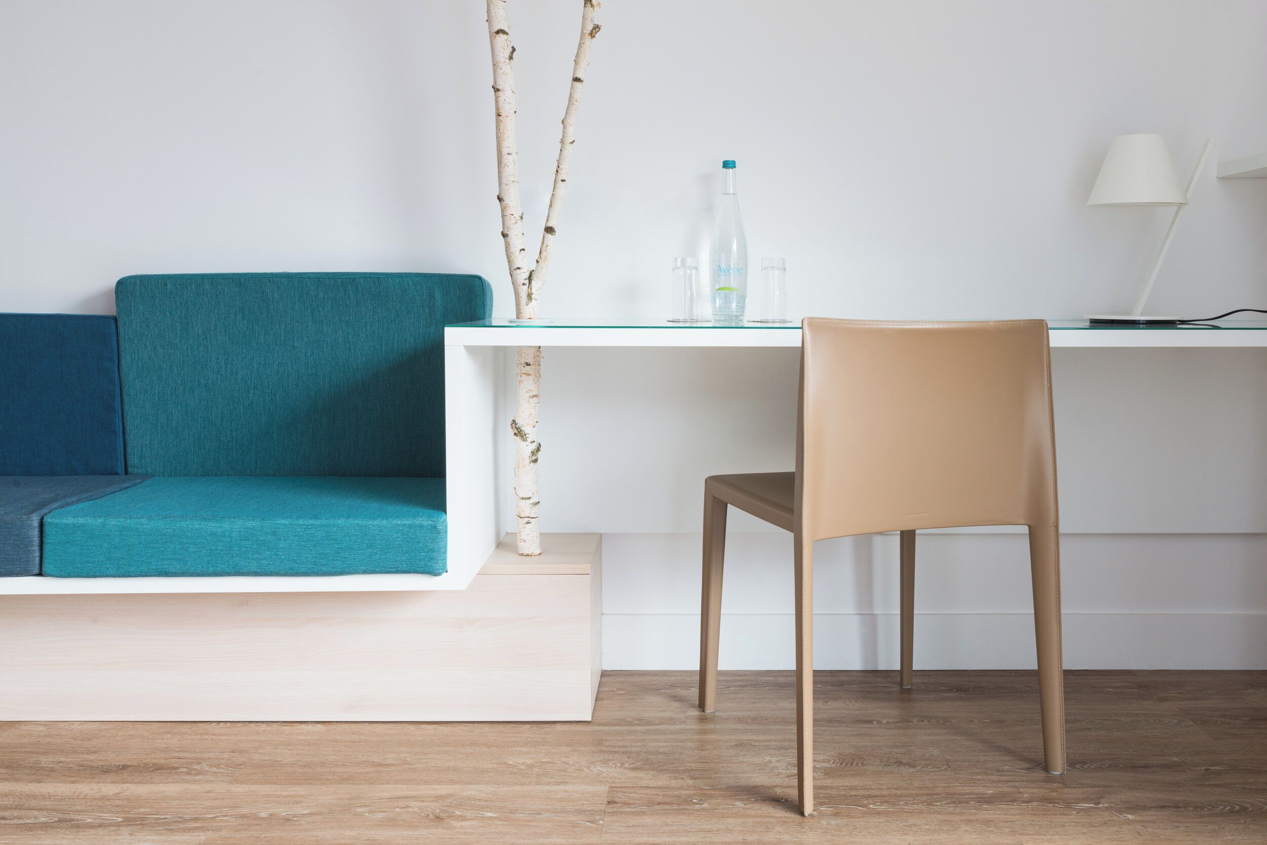 A modern room with a teal sofa, a wooden chair, a white desk, and a laptop.
