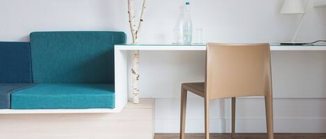 A modern room with a teal sofa, a wooden chair, a white desk, and a laptop.