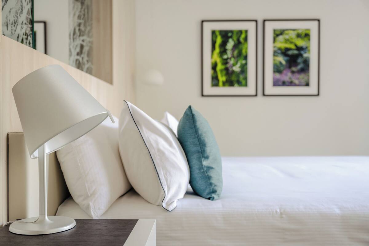 A neatly made bed with pillows, a bedside lamp, and framed pictures on the wall.