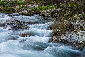 Un río fluye sobre rocas, con un paisaje rocoso y cubierto de hierba al fondo.