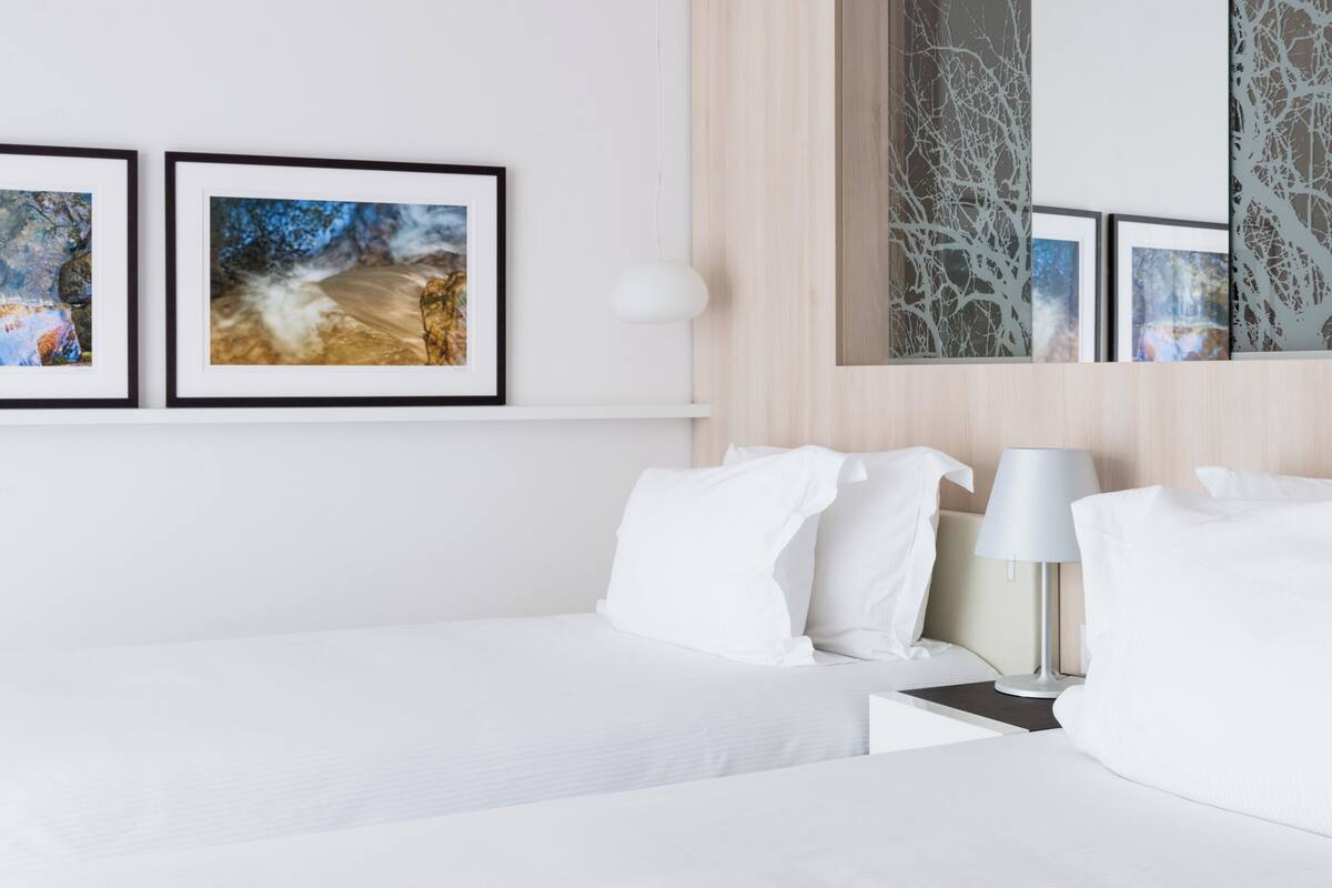 A hotel room with a neatly made bed, a bedside table with a lamp, and two framed pictures on the wall.
