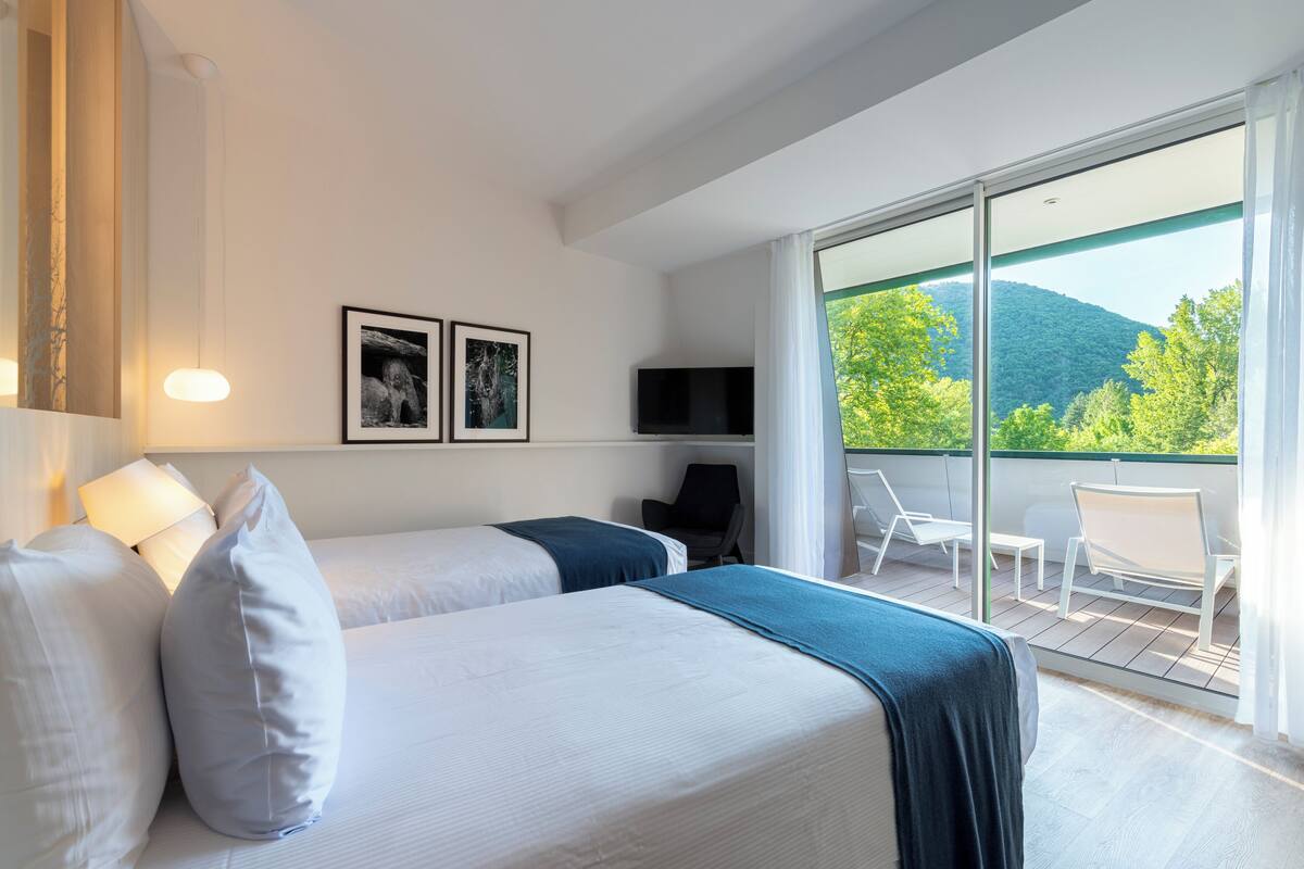 A hotel room with two beds, a TV, and a balcony with chairs and a table.
