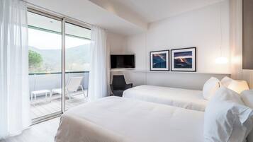 A modern hotel room with two beds, a TV, a chair, and a balcony with a view of the mountains.
