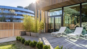 Uma área de estar moderna ao ar livre com deck de madeira, plantas em vasos e cadeiras de lounge brancas.