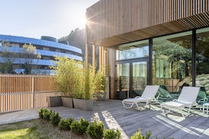 Un área de descanso al aire libre moderna con cubierta de madera, plantas en macetas y sillas de lounge blancas.